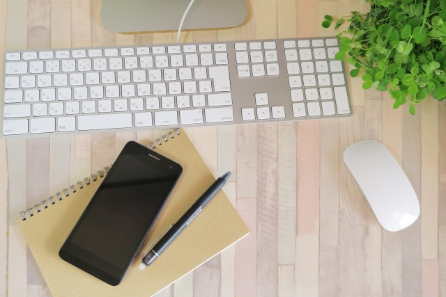 レンタルオフィスのデスクに置かれたキーボードとスマートフォン、ノートの作業環境