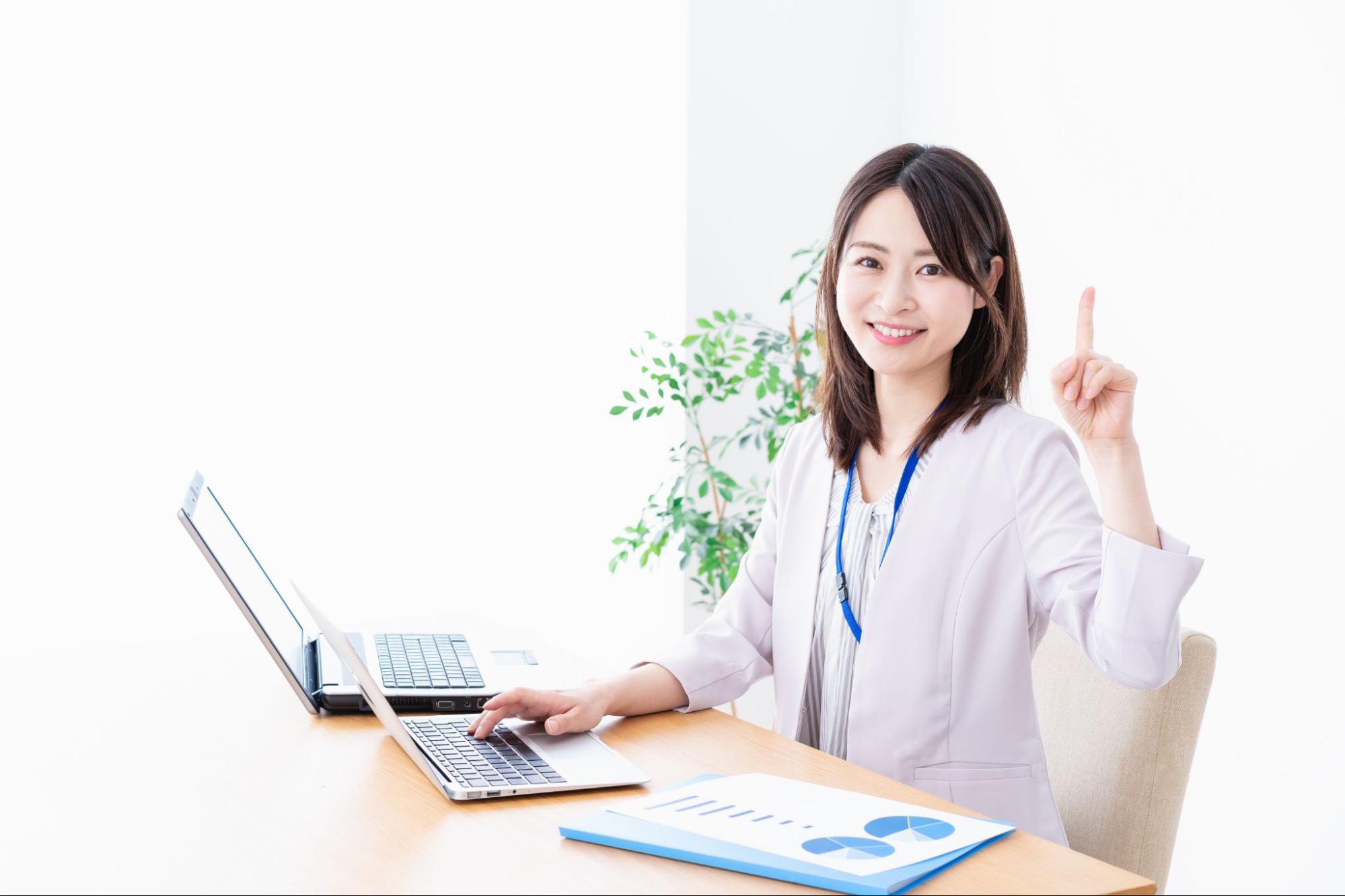 パソコンを操作しながら指を立てて説明する笑顔の女性スタッフ